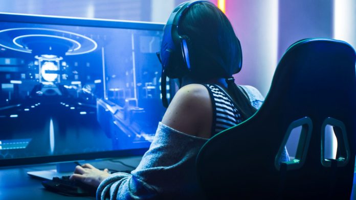 Pro Gamer Girl Playing in First-Person Shooter Online Video Game on Her Personal Computer. Casual Cute Geek wearing Glasses and Headset. Neon Room.
