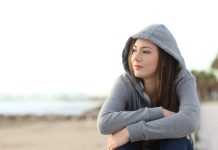 Portrait of a longing pensive teenager sitting on the beach looking away at the horizon