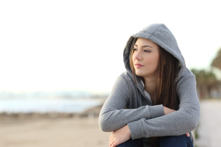 Portrait of a longing pensive teenager sitting on the beach looking away at the horizon